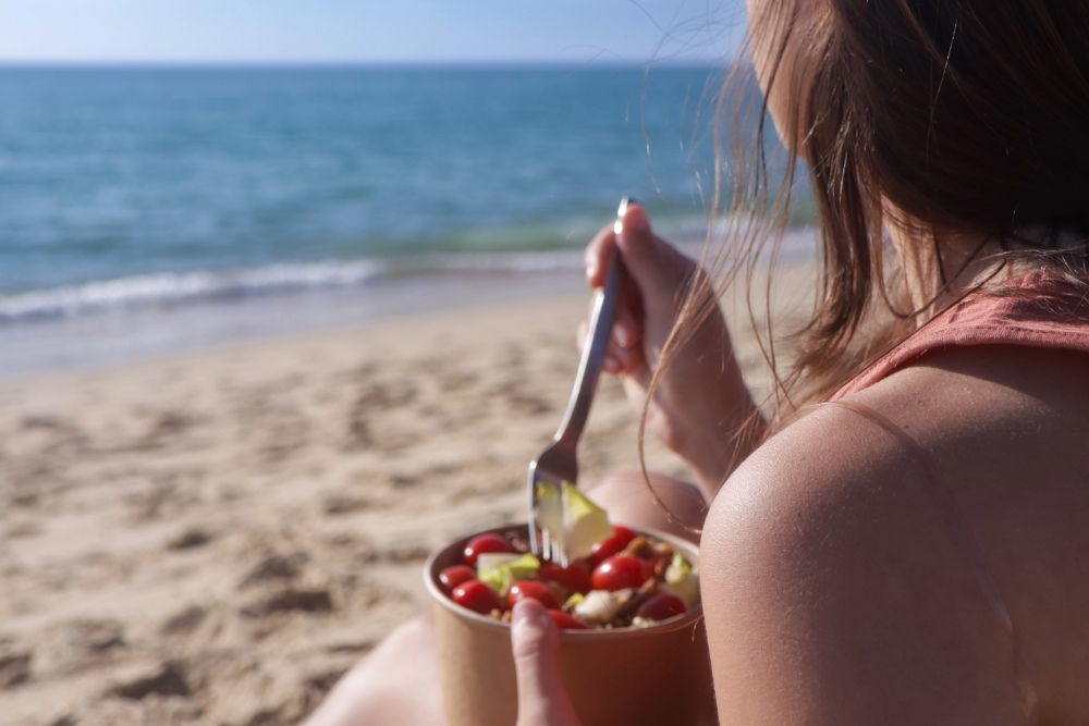 Young woman with dark hair enjoying a salad on the beach during summer.